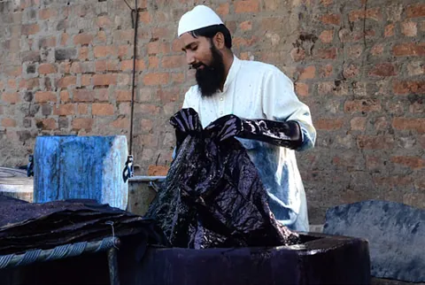 Artisan lifting indigo-dyed cloth from a dye vat at Ajrakhpur