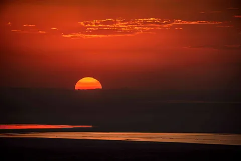 Red sun setting over the Great Rann, with salt pans shining in the foreground
