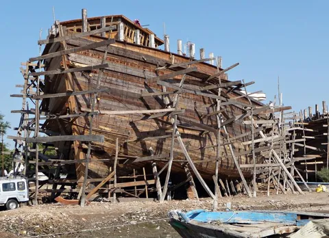 Wooden dhow under construction on scaffolding at a Mandvi shipyard