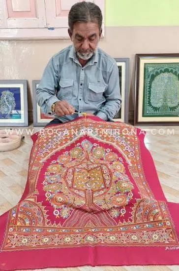 Artist painting a Rogan tree-of-life design on red cloth in Nirona