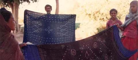 Villagers holding up dark woollen bandhani shawls with tie-dyed dot patterns