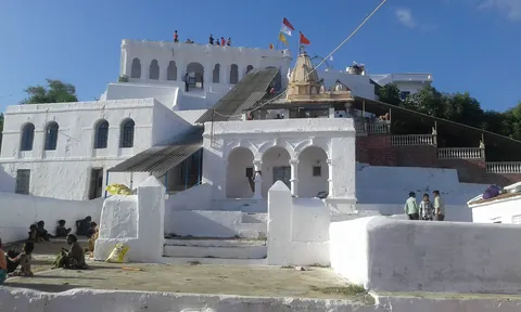 Whitewashed hilltop temple of Yaksh 72 with flags, and visitors on its terraces